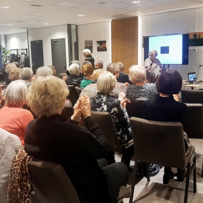 2023-12-15 - Voorzitter van de Kunstkring, Thea van Sunten, zette penningmeester/secretaris, Betty Leenaars, in het zonnetje tijdens de lezing over Schubert die gegeven werd door Karin Schade (rechts op de foto)